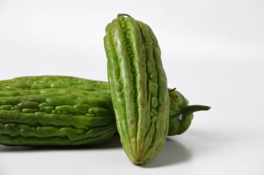 Endonezya yemeklerinde popüler bir tropikal sebze olan yeşil acı sukabaklarının kapağı temiz beyaz bir yüzey üzerinde taze ve izole bir şekilde sergilenmektedir..