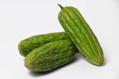 Endonezya yemeklerinde popüler bir tropikal sebze olan yeşil acı sukabaklarının kapağı temiz beyaz bir yüzey üzerinde taze ve izole bir şekilde sergilenmektedir..