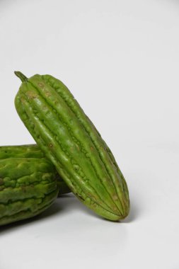 Endonezya yemeklerinde popüler bir tropikal sebze olan yeşil acı sukabaklarının kapağı temiz beyaz bir yüzey üzerinde taze ve izole bir şekilde sergilenmektedir..