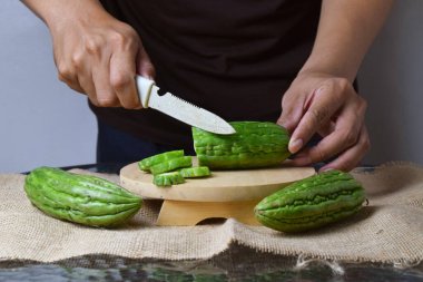Asyalı bir adamın elini, parmaklarıyla ahşap bir tabanda yeşil kavun keserken ve beyaz bir arka planı olan çuval bezi keserken yakın plan..