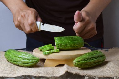 Asyalı bir adam yeşil kavunu kesiyor çuval bezinde ahşap bir taban ve izole beyaz bir zemin ile