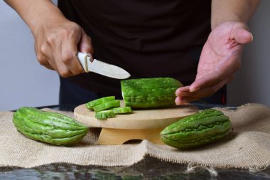 Asyalı bir adam yeşil kavunu kesiyor çuval bezinde ahşap bir taban ve izole beyaz bir zemin ile