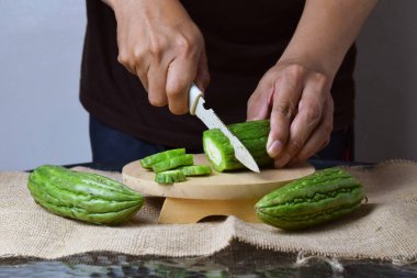 Asyalı bir adam yeşil kavunu kesiyor çuval bezinde ahşap bir taban ve izole beyaz bir zemin ile