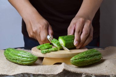 Asyalı bir adam yeşil kavunu kesiyor çuval bezinde ahşap bir taban ve izole beyaz bir zemin ile