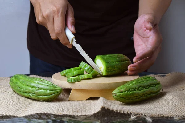 Asyalı bir adam yeşil kavunu kesiyor çuval bezinde ahşap bir taban ve izole beyaz bir zemin ile