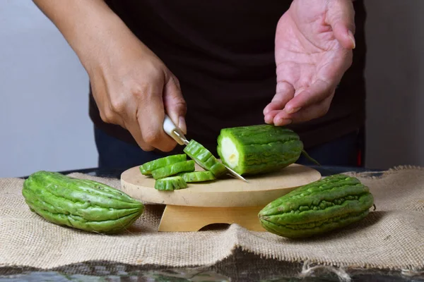 Asyalı bir adam yeşil kavunu kesiyor çuval bezinde ahşap bir taban ve izole beyaz bir zemin ile