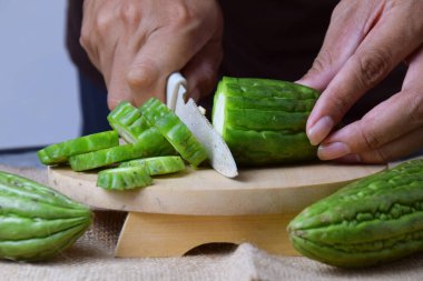 Çuval bezi ve izole edilmiş beyaz arkaplan üzerine ahşap tabanlı yeşil kavun kesen Asyalı bir adamın elini yakın plan çek..