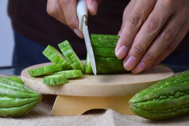 Çuval bezi ve izole edilmiş beyaz arkaplan üzerine ahşap tabanlı yeşil kavun kesen Asyalı bir adamın elini yakın plan çek..