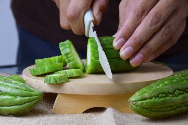 Çuval bezi ve izole edilmiş beyaz arkaplan üzerine ahşap tabanlı yeşil kavun kesen Asyalı bir adamın elini yakın plan çek..