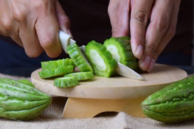 Çuval bezi ve izole edilmiş beyaz arkaplan üzerine ahşap tabanlı yeşil kavun kesen Asyalı bir adamın elini yakın plan çek..
