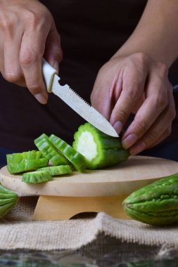 Çuval bezi ve izole edilmiş beyaz arkaplan üzerine ahşap tabanlı yeşil kavun kesen Asyalı bir adamın elini yakın plan çek..