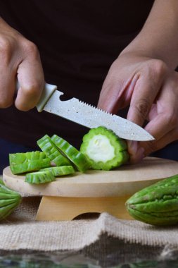 Çuval bezi ve izole edilmiş beyaz arkaplan üzerine ahşap tabanlı yeşil kavun kesen Asyalı bir adamın elini yakın plan çek..