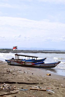 Cilacap, Endonezya - 18 Haziran 2025: Cilacap, Orta Java 'da yerel tekne ve turistlerin bulunduğu kumlu sahil manzarası.