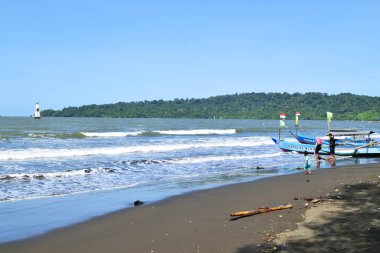 Cilacap, Endonezya - 18 Haziran 2025: Cilacap, Orta Java 'da yerel tekne ve turistlerin bulunduğu kumlu sahil manzarası.