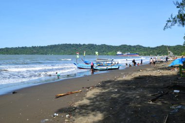 Cilacap, Endonezya - 18 Haziran 2025: Cilacap, Orta Java 'da yerel tekne ve turistlerin bulunduğu kumlu sahil manzarası.