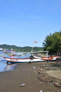 Cilacap, Endonezya - 18 Haziran 2025: Cilacap, Central Java, Endonezya 'da geniş bir kumsal manzarası, geleneksel balıkçı tekneleri, kıyıda bir hindistan cevizi ve uzak bir deniz feneri.