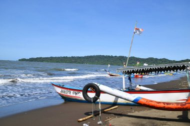 Cilacap, Endonezya - 18 Haziran 2025: Joker 1 adlı geleneksel bir balıkçı teknesi, Endonezya 'nın orta kesimindeki Cilacap sahilinde, açık mavi bir gökyüzünün altında demirledi..