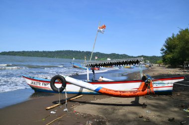 Cilacap, Endonezya - 18 Haziran 2025: Joker 1 adlı geleneksel bir balıkçı teknesi, Endonezya 'nın orta kesimindeki Cilacap sahilinde, açık mavi bir gökyüzünün altında demirledi..