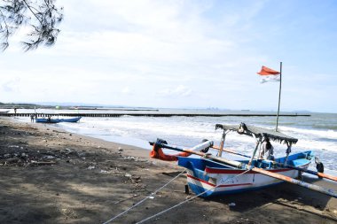 Cilacap, Endonezya - 18 Haziran 2025: Endonezya 'da Cilacap, Central Java, Endonezya' da plastik atıklarla dolu bir plaja demirlemiş geleneksel bir balıkçı teknesi.
