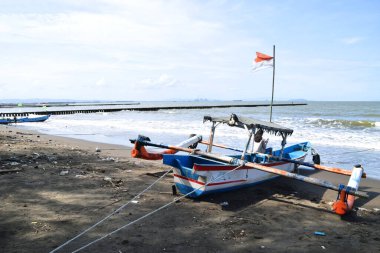 Cilacap, Endonezya - 18 Haziran 2025: Endonezya 'da Cilacap, Central Java, Endonezya' da plastik atıklarla dolu bir plaja demirlemiş geleneksel bir balıkçı teknesi.