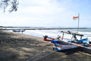 Cilacap, Endonezya - 18 Haziran 2025: Endonezya 'da Cilacap, Central Java, Endonezya' da plastik atıklarla dolu bir plaja demirlemiş geleneksel bir balıkçı teknesi.