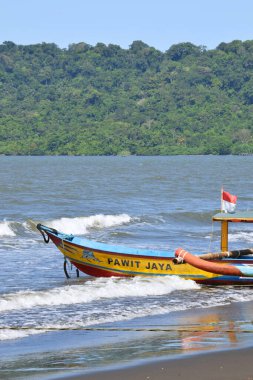 Kırmızı ve beyaz Endonezya bayrağının yer aldığı canlı bir geleneksel balıkçı teknesi, Cilacap, Central Java 'nın kumlu sahilinde demirli..