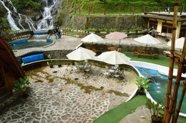 Purwokerto, Endonezya - 20 Haziran 2025: Geleneksel taş ve ahşap süslemeleri olan bir şelale yakınında bir doğa temalı restoran Purwokerto, Endonezya 'da yer almaktadır..