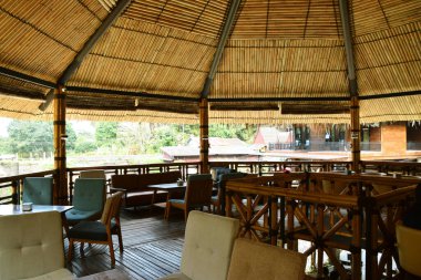 Geleneksel bambu mimarisi, ahşap zemin, rahat oturma alanı ve büyük konik bambu çatısının bulunduğu samimi bir restoran veya kafe manzarası..