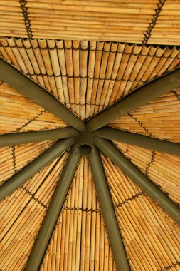Yeşil metal borularla desteklenen simetrik dairesel desenli doğal bambu direklerinden yapılmış geleneksel bir çardak tavanının düşük açılı görüntüsü..