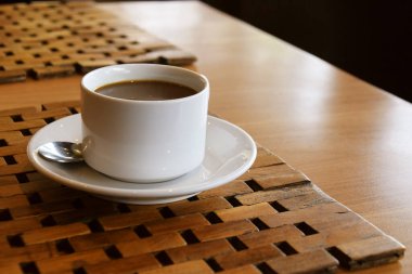 Endonezya 'nın Kuningan kentindeki bir kafede örülmüş ahşap bir paspasın üzerine gümüş kaşıkla beyaz bir fincan üzerinde bir fincan sade kahve..
