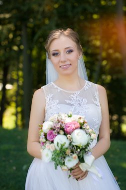 Beyaz gelinlik giymiş genç gelinin elinde güzel gelin buketi.