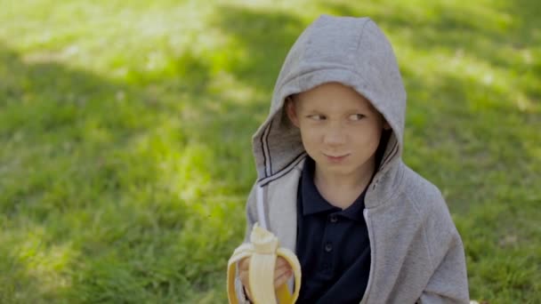 Ein süßer Junge isst eine Banane — Stockvideo
