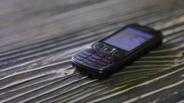 Old black cell phone isolated on a wooden background. — Stock Video