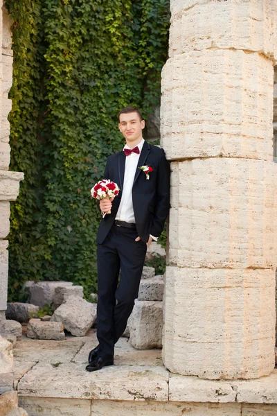 El novio sostiene una corbata y sonríe.Retrato del novio en el parque en el día de su boda. — Foto de Stock
