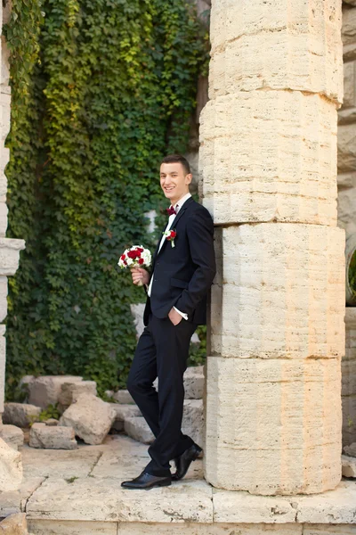 Der Bräutigam hält eine Krawatte und lächelt. Porträt des Bräutigams am Hochzeitstag im Park. — Stockfoto