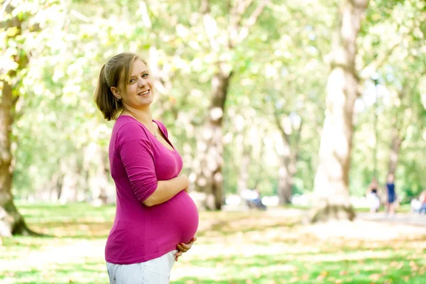 Happy and young pregnant woman in park in summer Stock Picture