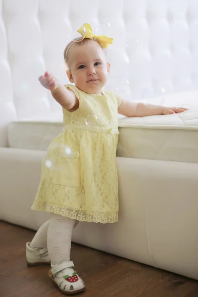 Niña en vestido amarillo la captura de burbujas de jabón — Foto de Stock