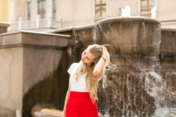 Счастливая молодая женщина с длинными волосами стоит у фонтана — стоковое фото