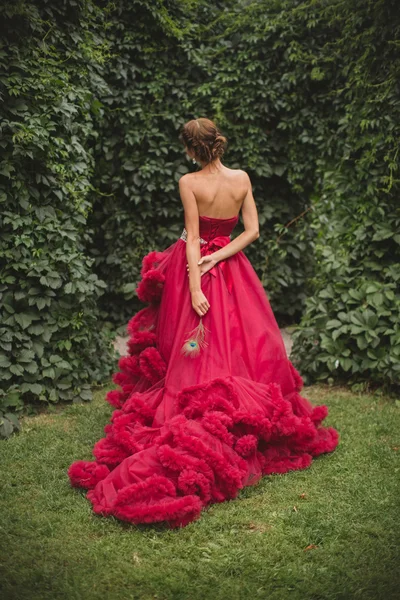 Menina bonita em um vestido longo no jardim. Pena de pavão — Fotografia de Stock