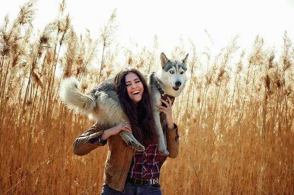 genç kadın ile onun Sibirya husky köpek yavrusu bir alanda gün batımı sırasında oynamaya. Mutlu gülümseyen kız açık havada güzel bir ışık having oyunculuk ile a köpek yavrusu. Onun omuzlarında tutar