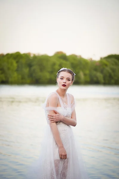 在白色的蕾丝服饰波西米亚风格的女孩站在靠近水的地方。看着相机 — 图库照片