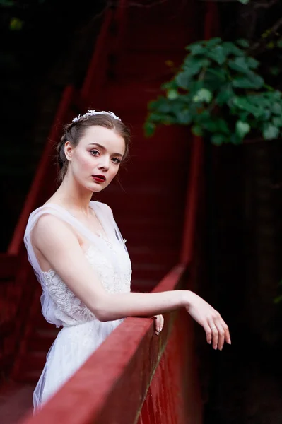 Genç güzel kız kameraya bakarak beyaz elbiseli kırmızı köprüdeki ayakta — Stok fotoğraf