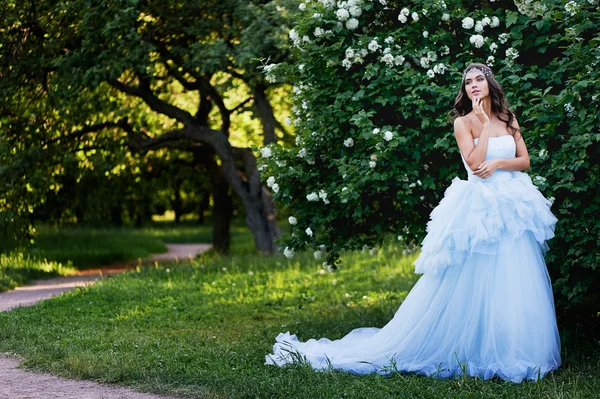 Brunetka w bujnej niebieska sukienka z pięknych włosów siedzi na rzece stones.her duży Bank usytuowany jest w ogrodzie — Zdjęcie stockowe