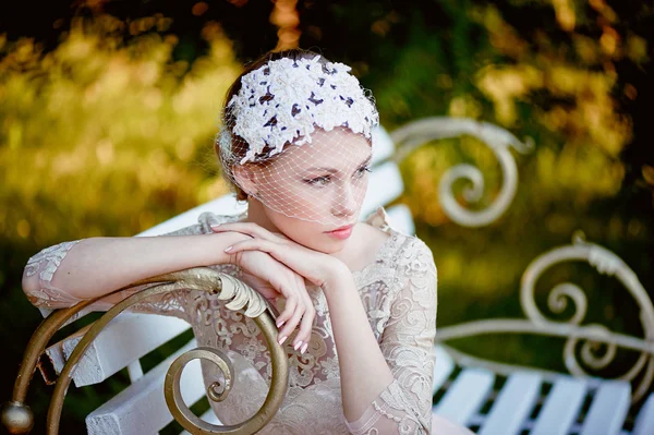 Hermosa rubia con un peinado y velo sentado en el banco, looks románticos —  Fotos de Stock