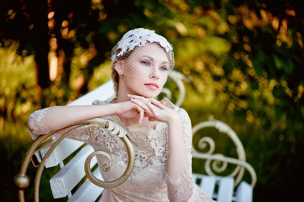 Blonde avec une coiffure et un voile assis sur le banc, regards romantiques — Photo