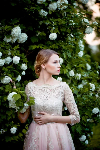 Hübsche zarte Blondine in einem Spitzenkleid vor dem Hintergrund eines blühenden Gartens — Stockfoto