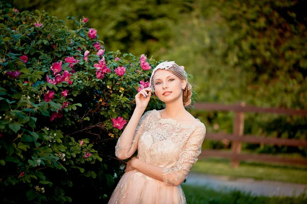 Bella bionda tenera in un abito di crema di pizzo sullo sfondo del giardino fiorito — Foto Stock