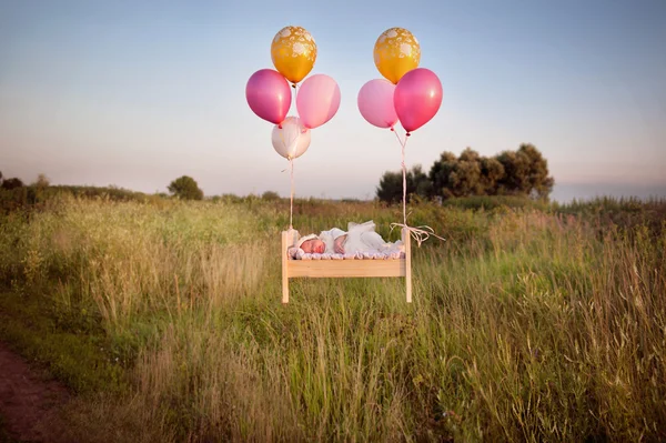 Malé dítě spát v postýlce v krajkové kapoty A v čepici a letí pryč s balónky — Stock fotografie