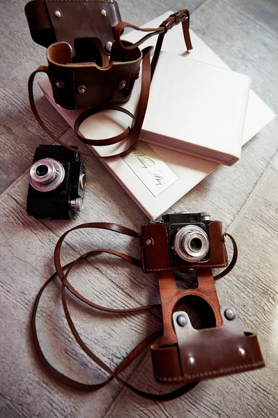 Яркая фотокнига с кожаной легкой крышкой, лежащая на полу. Следующие две камеры в коричневом ящике — стоковое фото