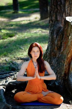 Young beautiful red-haired girl does yoga in Park on green background. .